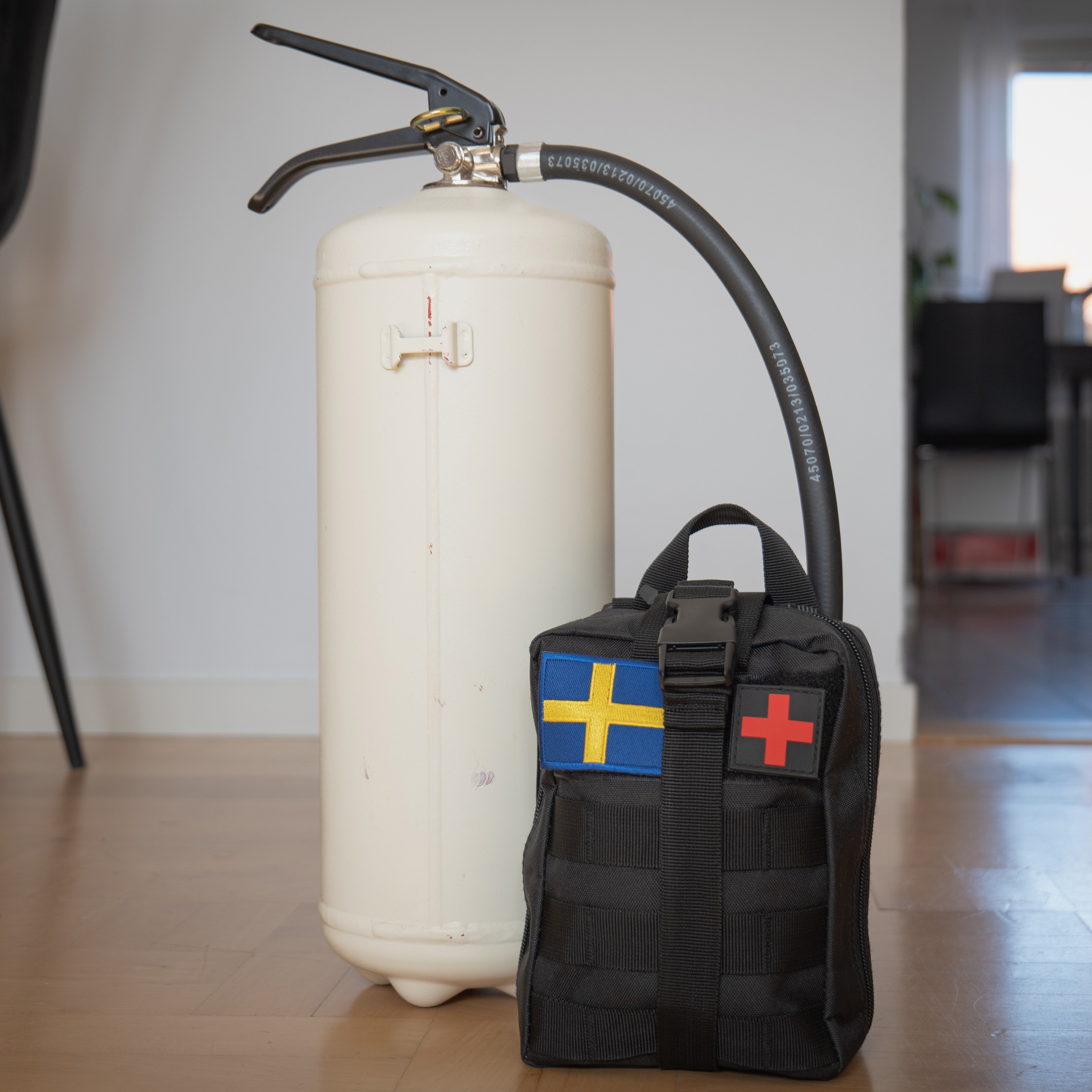 A survival kit next to a fire extinguisher, placed on a wooden floor in an indoor setting